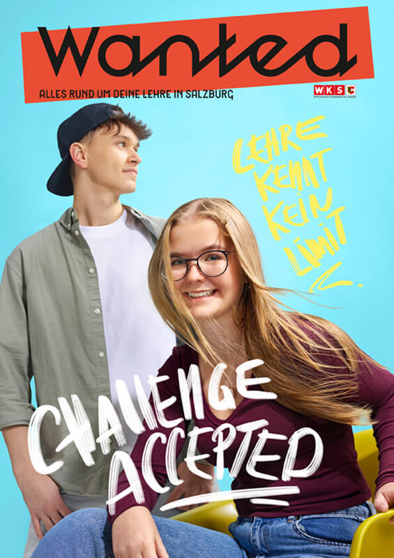 Zwei Personen posieren lächelnd vor einem „Wanted“-Plakat mit dem Text „Challenge accepted“. Sie tragen Business-Kleidung und halten ein Schild mit demselben Spruch. Das Plakat wirkt wie ein lustiges oder motivierendes Poster.